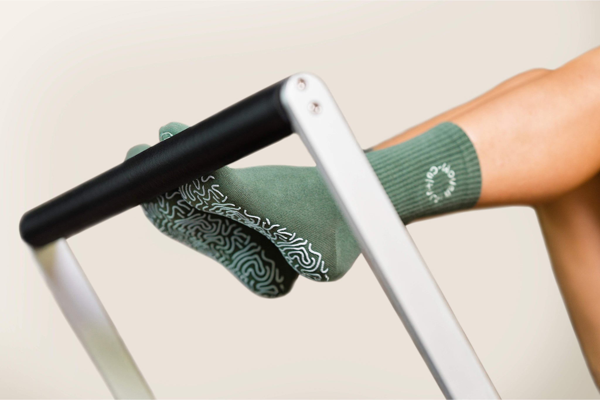Moss green organic cotton grip socks on Pilates reformer footbar – non-slip sole pattern.