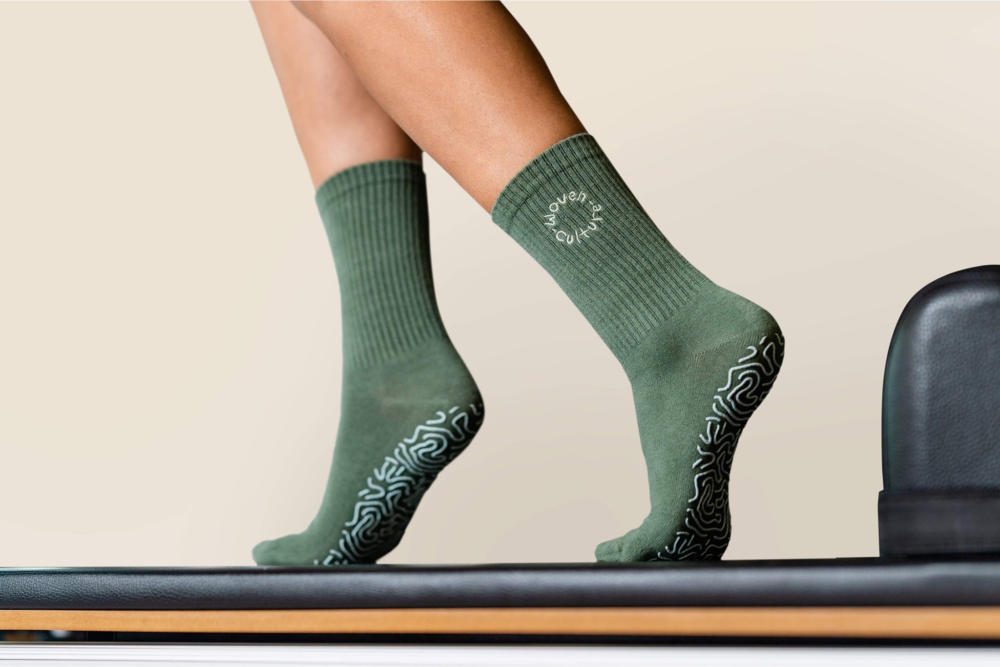 Close-up of Moss green organic cotton grip socks on reformer bar – non-slip sole pattern by Woven Culture.